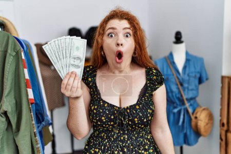 Photo for Young redhead woman holding shopping bags and dollars scared and amazed with open mouth for surprise, disbelief face - Royalty Free Image