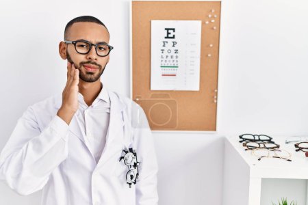 Photo for African american optician man standing by eyesight test touching mouth with hand with painful expression because of toothache or dental illness on teeth. dentist - Royalty Free Image