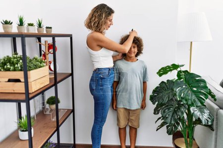 Téléchargez les photos : Mère et fils mesurant la marque de dessin en hauteur de l'enfant sur le mur à la maison - en image libre de droit