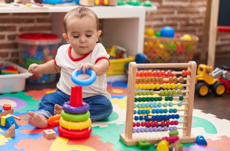 Entzückendes hispanisches Baby, das mit Abakus und Reifen spielt, sitzt im Kindergarten auf dem Boden