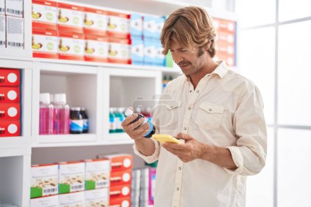 Téléchargez les photos : Jeune homme client utilisant smartphone tenant bouteille de médicament à la pharmacie - en image libre de droit