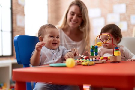 Foto de Profesor y estudiantes de preescolar jugando con juguetes sentados en la mesa en el jardín de infantes - Imagen libre de derechos