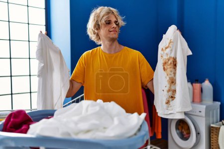 Photo for Young man holding clean white t shirt and t shirt with dirty stain smiling looking to the side and staring away thinking. - Royalty Free Image