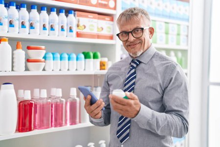 Photo for Middle age grey-haired man customer using smartphone holding medicine bottle at laboratory - Royalty Free Image