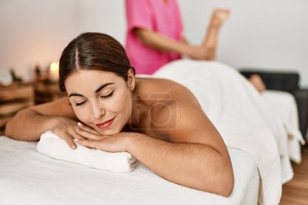 Téléchargez les photos : Jeune belle femme hispanique allongée sur la table ayant massage des jambes au salon de beauté - en image libre de droit