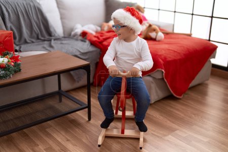 Photo for Adorable hispanic toddler wearing christmas hat playing with reindeer rocking at home - Royalty Free Image