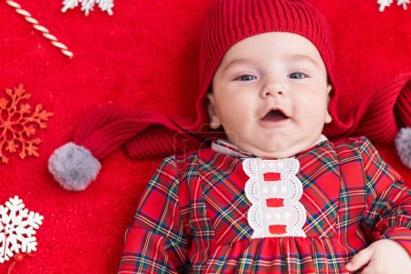 Foto de Adorable bebé caucásico acostado en el suelo con decoración de Navidad sobre fondo rojo aislado - Imagen libre de derechos