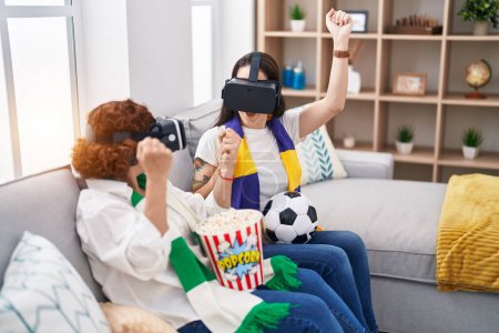 Photo for Two women mother and daughter watching soccer match using vr glasses at home - Royalty Free Image