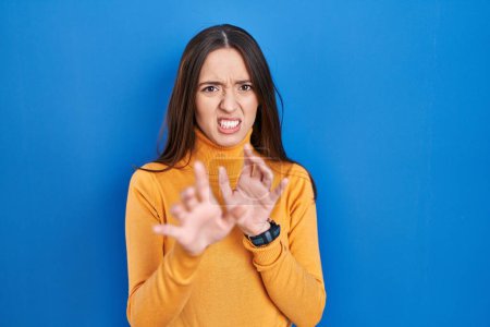 Photo for Young brunette woman standing over blue background disgusted expression, displeased and fearful doing disgust face because aversion reaction. - Royalty Free Image