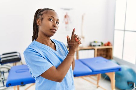 Téléchargez les photos : Femme noire avec des tresses travaillant à la clinique de récupération de la douleur tenant une arme symbolique avec geste de la main, jouant à tuer les armes à feu, visage en colère - en image libre de droit
