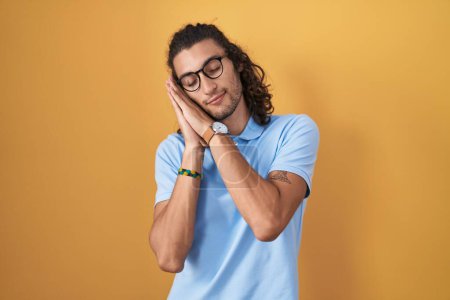 Téléchargez les photos : Young hispanic man standing over yellow background sleeping tired dreaming and posing with hands together while smiling with closed eyes. - en image libre de droit
