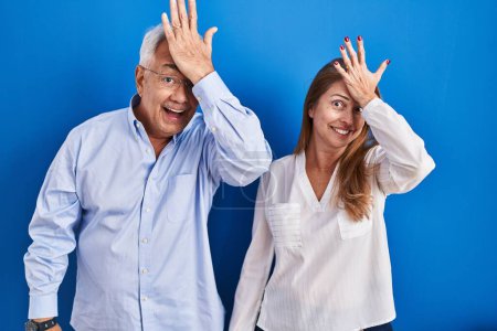 Photo for Middle age hispanic couple standing over blue background surprised with hand on head for mistake, remember error. forgot, bad memory concept. - Royalty Free Image