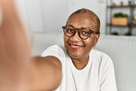 Foto de Senior africana americana mujer hacer selfie por la cámara sentado en sofá en casa - Imagen libre de derechos