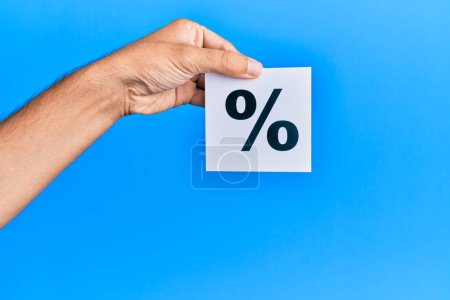 Photo for Hand of caucasian man holding paper with percentage mark over isolated blue background - Royalty Free Image