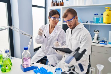 Photo for Man and woman scientist partners write on clipboard holding test tube working at laboratory - Royalty Free Image