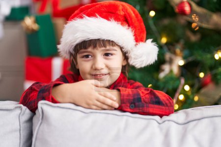 Foto de Adorable niño sonriendo confiado de pie junto al árbol de Navidad en casa - Imagen libre de derechos
