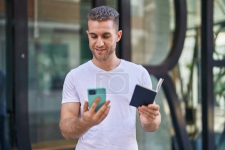 Téléchargez les photos : Jeune homme caucasien utilisant smartphone tenant passeport à la rue - en image libre de droit