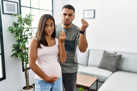 Foto de Joven pareja interracial esperando un bebé, tocando el vientre embarazada haciendo gesto italiano con la mano y los dedos expresión confiada - Imagen libre de derechos
