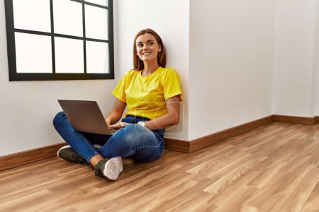Photo for Young woman using laptop sitting on floor at empty room - Royalty Free Image