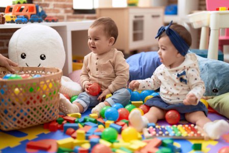 Téléchargez les photos : Deux tout-petits jouant avec des boules et un xylophone assis sur le sol à la maternelle - en image libre de droit