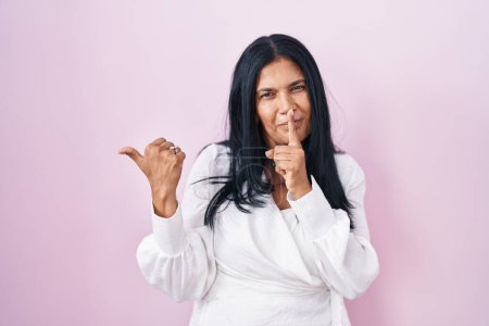 Téléchargez les photos : Mature hispanic woman standing over pink background asking to be quiet with finger on lips pointing with hand to the side. silence and secret concept. - en image libre de droit