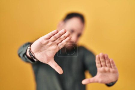 Téléchargez les photos : Plus taille homme hispanique avec barbe debout sur fond jaune faisant cadre à l'aide de mains paumes et doigts, perspective de la caméra - en image libre de droit