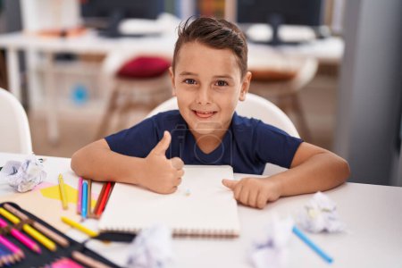 Foto de Adorable estudiante hispano niño sonriendo confiado haciendo buen gesto con el dedo en el aula - Imagen libre de derechos