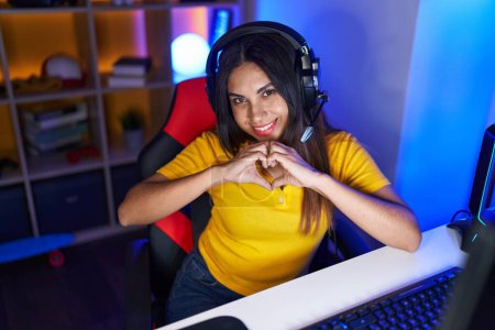 Téléchargez les photos : Jeune belle femme arabe banderole souriant confiant faire symbole de coeur avec les mains à la salle de jeux - en image libre de droit