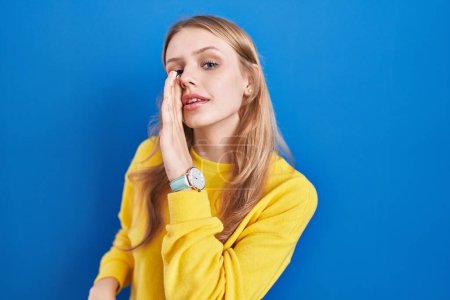 Photo for Young caucasian woman standing over blue background hand on mouth telling secret rumor, whispering malicious talk conversation - Royalty Free Image