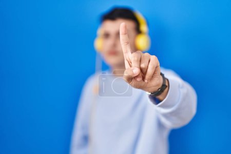Téléchargez les photos : Non binary person listening to music using headphones pointing with finger up and angry expression, showing no gesture - en image libre de droit