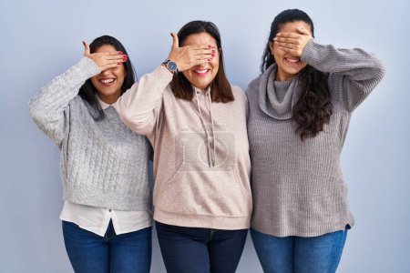 Foto de Mother and two daughters standing over blue background smiling and laughing with hand on face covering eyes for surprise. blind concept. - Imagen libre de derechos