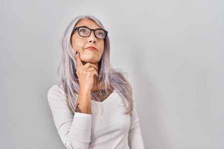 Photo for Middle age woman with grey hair standing over white background with hand on chin thinking about question, pensive expression. smiling with thoughtful face. doubt concept. - Royalty Free Image