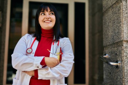 Photo for Young brunette woman wearing doctor uniform and stethoscope at house entrance - Royalty Free Image