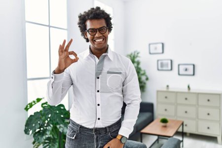 Photo for African psychologist man at consultation office smiling positive doing ok sign with hand and fingers. successful expression. - Royalty Free Image