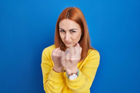 Téléchargez les photos : Jeune femme debout sur fond bleu prêt à se battre avec geste de défense poing, visage en colère et bouleversé, peur du problème - en image libre de droit