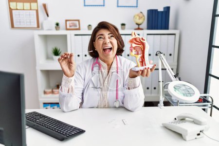 Photo for Middle age hispanic doctor woman holding coronavirus infection nasal test angry and mad screaming frustrated and furious, shouting with anger looking up. - Royalty Free Image