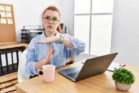 Foto de Young redhead woman working at the office using computer laptop doing time out gesture with hands, frustrated and serious face - Imagen libre de derechos
