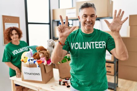 Photo for Middle age man wearing volunteer t shirt at donations stand showing and pointing up with fingers number eight while smiling confident and happy. - Royalty Free Image