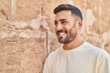 Téléchargez les photos : Jeune homme hispanique souriant confiant regardant sur le côté sur fond de pierre isolée - en image libre de droit