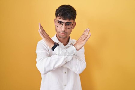 Photo for Young hispanic man standing over yellow background rejection expression crossing arms doing negative sign, angry face - Royalty Free Image