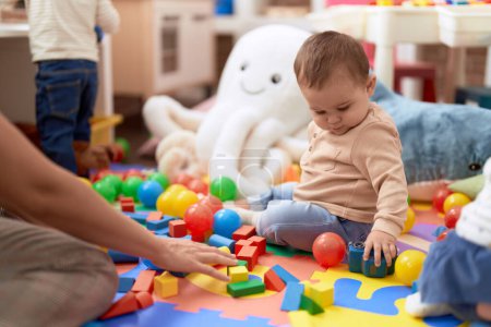 Foto de Adorable niño jugando con juguetes sentados en el suelo en el jardín de infantes - Imagen libre de derechos