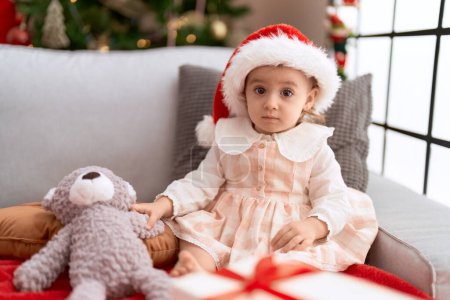 Photo for Adorable caucasian girl sitting on sofa by christmas tree at home - Royalty Free Image