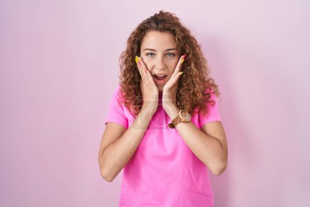 Téléchargez les photos : Jeune femme caucasienne debout sur fond rose effrayée et choquée, surprise et expression étonnante avec les mains sur le visage - en image libre de droit