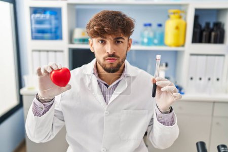 Foto de Arab man with beard working at scientist laboratory holding blood samples skeptic and nervous, frowning upset because of problem. negative person. - Imagen libre de derechos