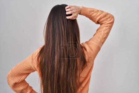 Téléchargez les photos : Jeune femme brune debout sur fond blanc vers l'arrière pensant au doute avec la main sur la tête - en image libre de droit