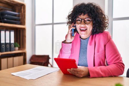 Foto de Joven hermosa mujer hispana trabajadora de negocios hablando en smartphone usando touchpad en la oficina - Imagen libre de derechos