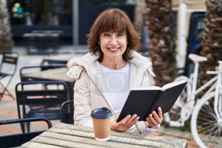 Photo for Middle age woman reading book sitting on table at coffee shop terrace - Royalty Free Image