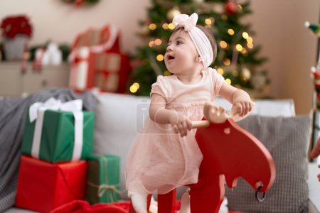 Photo for Adorable toddler playing on rocking reindeer by christmas tree at home - Royalty Free Image