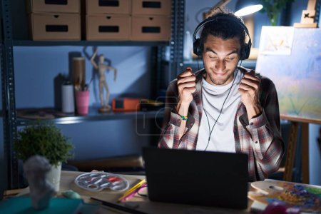 Photo for Young hispanic man sitting at art studio with laptop late at night excited for success with arms raised and eyes closed celebrating victory smiling. winner concept. - Royalty Free Image