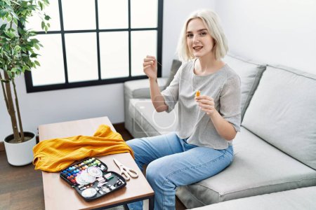 Photo for Young caucasian woman smiling confident sewing using needle and thread at home - Royalty Free Image